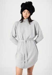 Vestido de malha cinza com um colarinho alto, cintura ajustada por um cinto e mangas longas em forma de asa de morcego. Apresenta uma textura suave e uma silhueta descontraída. Chapéu de pele preto.