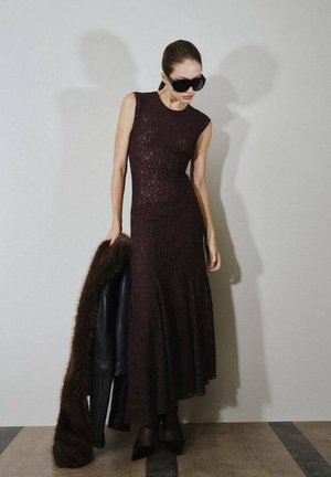 Larga vestido de encaje burdeos con un corpiño ajustado, dobladillo acampanado y diseño sin mangas. Combinado con una chaqueta de cuero negra con detalles de piel y tacones negros.