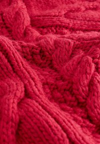 Grove, rood gebreide stof met een gestructureerd, verweven patroon. Het materiaal lijkt zacht en warm, met zichtbare vezels en steken.
