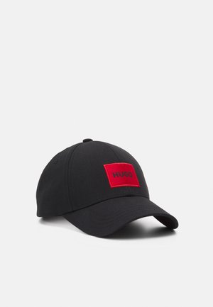 Casquette de baseball noire avec une visière courbée et un patch rectangulaire rouge affichant le mot « HUGO » en lettres noires.