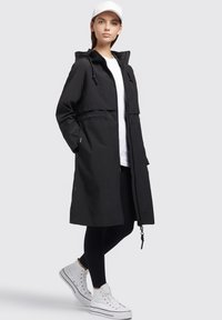 Veste noire à capuche avec fermeture éclair à l'avant, taille cintrée et manches longues. Comprend des poches latérales et une texture de tissu lisse et léger.