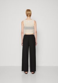 Krátký krémový krajkový top s vzorovanými detaily, kombinovaný s černými širokými kalhotami. Hladký povrch a prodyšná tkanina.