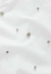 Un tissu blanc présentant divers strass ronds et transparents de différentes tailles dispersés sur la surface, créant un effet décoratif et texturé.