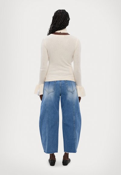 Maglione beige a maglia con corpetto aderente, dettagli con maniche a campana, abbinato a jeans in denim leggeri a vita alta e gamba larga con una finitura sbiadita.