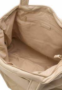 Interno di una borsa a spalla beige trapuntata con foderatura in tessuto liscio e tasca con zip; design minimalista, senza motivi o dettagli visibili.