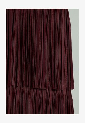 Gros plan sur un tissu plissé de couleur bordeaux foncé, avec des plis verticaux et une apparence douce et texturée sur un fond clair.