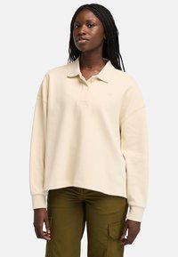 Krémové oversized polo svetrové tričko s klasickým límcem, krátkým zapínáním na knoflíky a pružnými manžetami, spárované s olivovými cargo kalhotami.