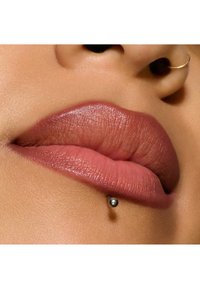 Närbild av fylliga läppar i en matt, rosa-brun nyans, med en silverfärgad labret-stud och slät hudstruktur.