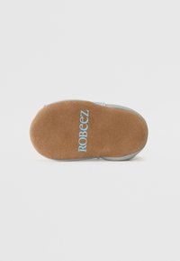Suela de zapato de ante con textura marrón claro, que presenta "ROBEEZ" en letras azul claro. Forma redondeada con un borde para mayor flexibilidad.
