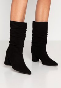 Czarne zamszowe botki za kostkę z luźnym krojem, spiczastym noskiem i blokowym obcasem. Gładka textura i minimalna ilość detali.