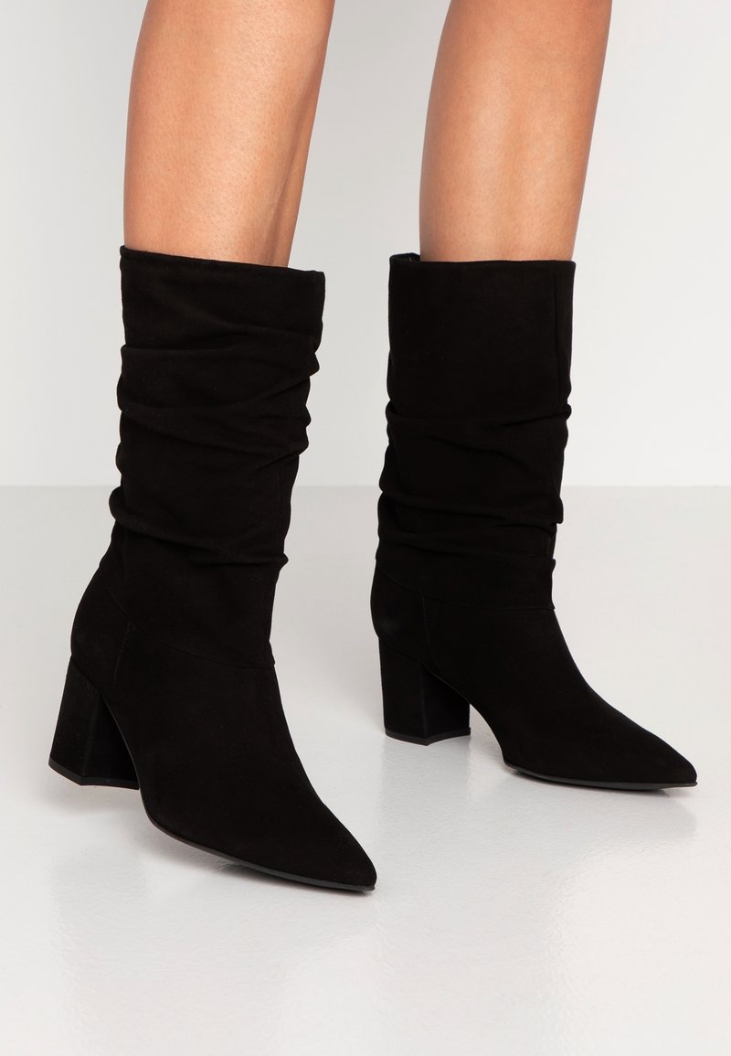 Czarne zamszowe botki za kostkę z luźnym krojem, spiczastym noskiem i blokowym obcasem. Gładka textura i minimalna ilość detali.