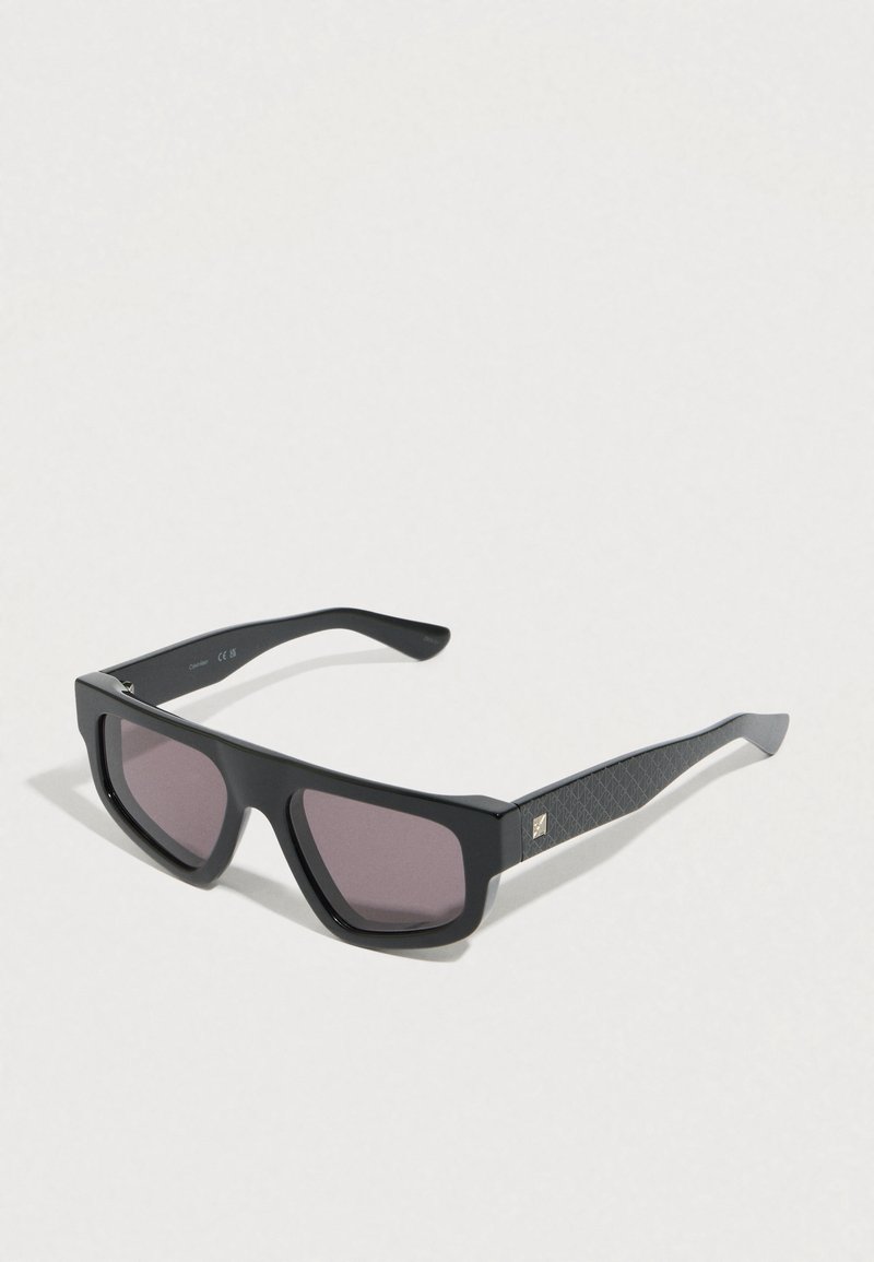 Gafas de sol cuadradas negras con montura gruesa, lentes moradas y varillas negras texturizadas que presentan un pequeño detalle de logo.