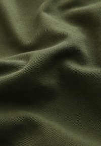 Gros plan d'un tissu vert avec une texture visible et des plis doux créant des ombres et des reflets délicats.