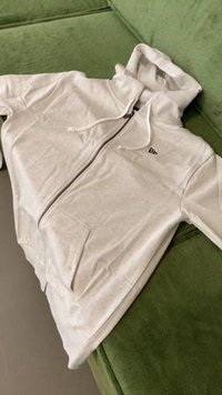 Svijetlo siva zip-up dukserica, izrađena od mekanog pamuka, s prednjim džepom, kapuljačom na vezanje i malim logotipom na grudima.