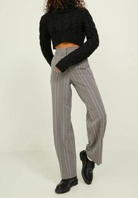 Czarny sweter o splotach warkoczowych z krótkim stanem i wysokim kołnierzem, zestawiony z szerokimi spodniami w kratę o wysokim stanie oraz czarnymi sznurowanymi butami.