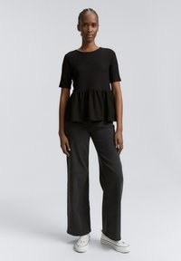 Haut peplum noir à côtes avec des manches courtes, associé à un jean large foncé et des baskets blanches. Design simple avec un tissu texturé.