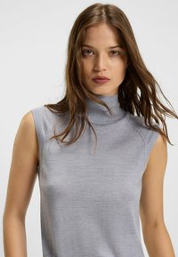 Top senza maniche di colore grigio chiaro, realizzato in un materiale morbido e testurizzato, con una leggera costina e una silhouette aderente.