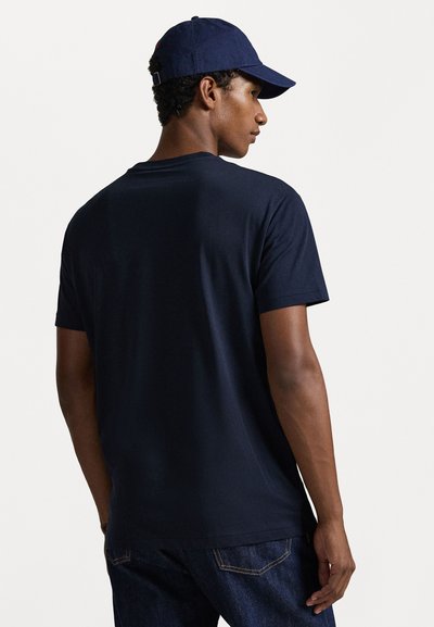 T-shirt de algodão azul marinho com gola redonda e mangas curtas, combinado com jeans escuros. A camisa apresenta uma textura suave e um corte relaxado.