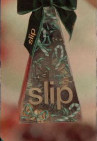 En gjennomsiktig trekantet boks med flerfargede hårstrikker i forskjellige teksturer. Pyntet med en mørkegrønn båndsløyfe og "slip"-logo.