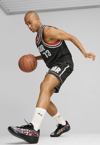 Maglietta da basket nera con scritte bianche "ROAR 73", abbinata a pantaloni corti neri. Il giocatore indossa scarpe da ginnastica nere e rosse a motivo e calze bianche.