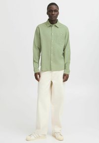 Light green long-sleeve button-up shirt with a chest pocket, paired with cream-colored wide-leg pants and light sneakers.