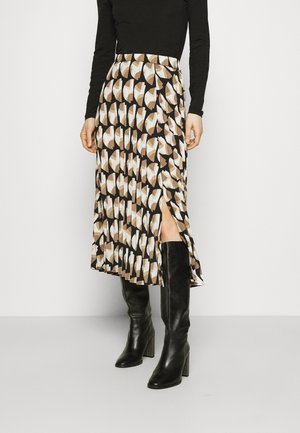 Jupe mi-longue avec un motif géométrique marron, beige et blanc, dotée d'une fente sur le côté, associée à des bottes en cuir noires montantes.
