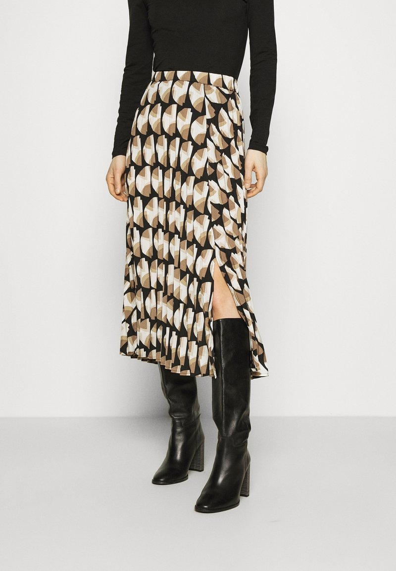 Keskipitkä hame ruskean, beigen ja valkoisen geometrisen kuvion kanssa, jossa on sivuaukko, yhdistettynä polven ylle ulottuviin mustiin nahkasaappaisiin.