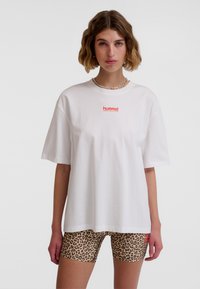 Hvid oversized t-shirt med "hummel"-logo i rødt, kombineret med beige cykelshorts med leopardprint. Enkel design, korte ærmer og afslappet pasform.