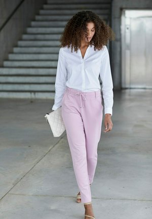 Witte overhemd met knopen, roze drawstring broek, beige slippers en een gewatteerde witte handtas. Glad materiaal met een relaxte pasvorm.