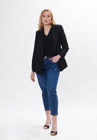 Sorte dobbeltbrystet blazer over en sort top med blondekant, parret med blå smalle jeans og sorte åbne hæle. Enkle accessories anvendt.