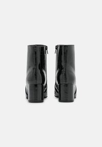 Botas negras hasta el tobillo con una textura brillante y estampado de cocodrilo. Presentan una punta redondeada y un tacón grueso. Cremalleras laterales para facilitar su uso.