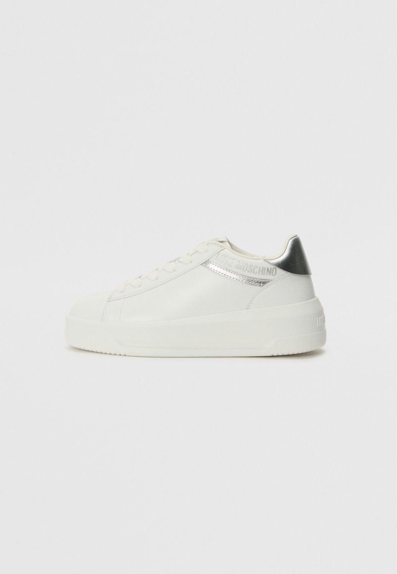 Sneaker bianca in pelle con un accento argento sul tallone e una striscia lucida. Presenta una suola piatta e chiusura con lacci. La superficie testurizzata aggiunge dettaglio.