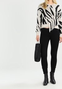 Černobílé pruhované pletené svetr s střapci na lemu, spárovaný s černými skinny džíny a kotníkovými botami. Drží černou kabelku.