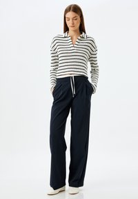 Gestreepte, cropped trui in wit en marineblauw met een polo-kraag, gecombineerd met hoge, losse marineblauwe broeken en witte sneakers.