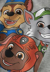 Szary materiał z kolorowymi, kreskówkowymi psami. Psy noszą różne tematyczne stroje w wyraźnych kolorach, w tym niebieskim, pomarańczowym i zielonym.