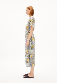 Luftiges, langes Kleid aus weichem Stoff mit einem mehrfarbigen Blumenmuster, mit kurzen Ärmeln und einer lockeren Silhouette. Getragen mit dunklen Slipper-Sandalen.