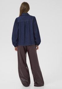 Dark denim blouse with puffed sleeves, a ruffled collar, and a slightly loose fit, paired with high-waisted, glossy brown leather pants.