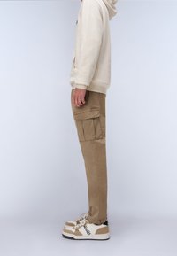 Beige sweatshirt med hætte, parret med tan cargo bukser med sidelommer og hvide sneakers med beige accenter og logo.