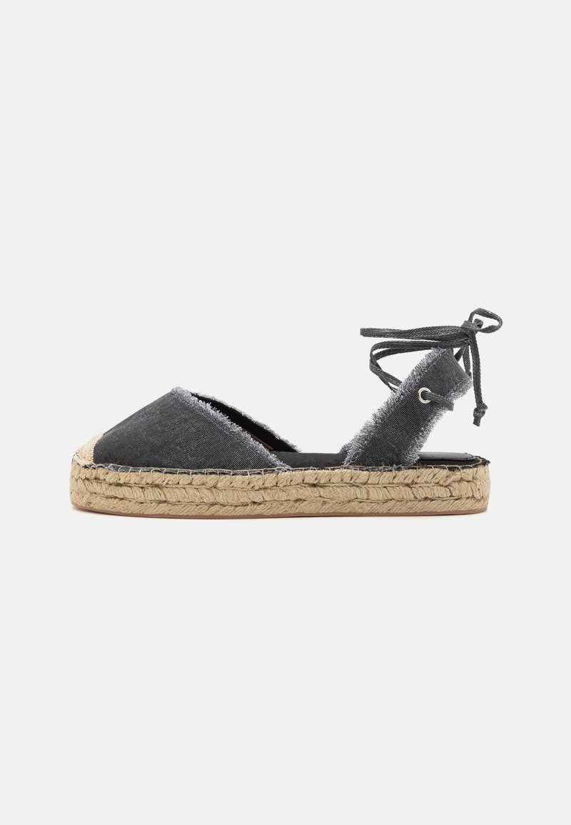 Sandalo espadrille in denim nero con bordi sfrangiati, lacci da avvolgere alla caviglia e suola platform in juta intrecciata su sfondo bianco.
