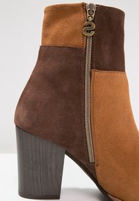 Bottine en daim bicolore avec talon bloc et fermeture éclair latérale dotée d'une tirette ronde en métal portant la marque "Desigual".