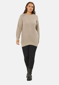 Beżowy sweter prążkowany z okrągłym dekoltem, długimi rękawami i luźnym krojem, w połączeniu z dopasowanymi czarnymi spodniami i czarnymi botkami za kostkę.