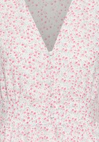 Robe en tissu blanc avec petit motif de fleurs roses, col en V et boutons couverts à l'avant.