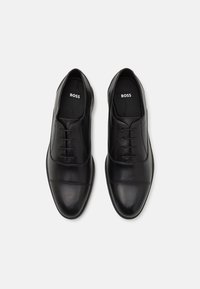 Pantofi din piele neagră cu o finisare netedă, design cu șireturi, vârf rotund și un accent cusut pe partea din față. Interiorul prezintă logo-ul brandului.