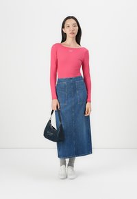 Rozā garām piedurknēm tops, zila džinsa maxi svārki ar divām priekšējām kabatām, pelēkas zeķes, baltas kedas un maza melna rokassoma.