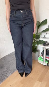 Visoko pasovi temno modri denim hlače z razširjeno nogo, z sprednjimi žepi in zlatimi šivi, v kombinaciji s črnimi čevlji na špic.