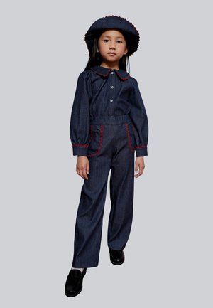 Conjunto de mezclilla con blusa de manga larga y cuello, pantalones anchos a juego y un sombrero redondo. Detalles en rojo en los bolsillos y el dobladillo que añaden un toque especial.