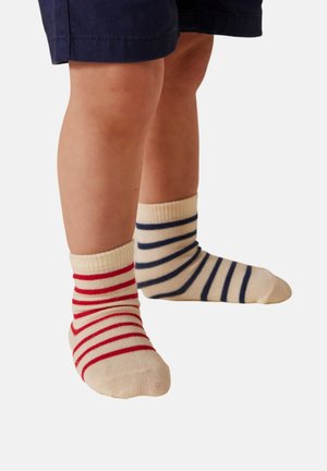 Gestreifte Knöchelsocken: eine mit roten Streifen auf cremigem Hintergrund, die andere mit marineblauen Streifen. Strickmaterial, gerippte Bündchen, klassischer Sockenstil.
