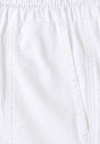 Gros plan sur un pantalon en tissu blanc avec une ceinture élastique et des détails de couture sur la poche latérale.