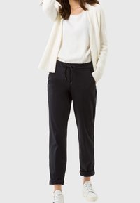 Czarne, dopasowane spodnie z elastycznym pasem, z podwiniętymi nogawkami i bocznymi kieszeniami, zestawione z białą bluzką i kremowym kardiganem.