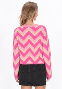 En fluffig tröja med mönster i rosa och gult chevron, med l�ång ärm, som bärs över en svart denimkjol. Tröjan har en avslappnad passform och rundad halsringning.